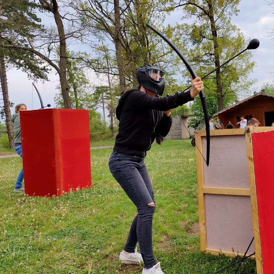 Arrowtag-Spielerin mit Schutzmaske spannt ihren Bogen neben einer roten Deckung.