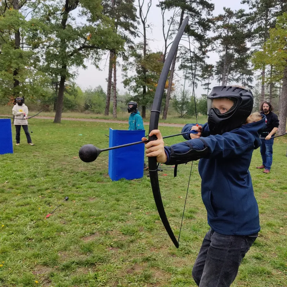 Arrowtag-Spielerin mit Schutzmaske spannt einen Bogen mit Schaumstoffpfeil im Freien.
